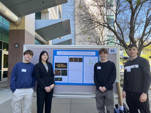 Two students stand on both the left and right sides of a wide research poster.